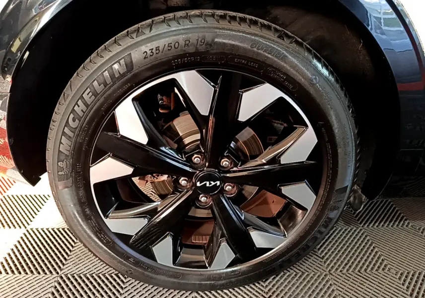 Gros plan sur la jante noire et argentée avec logo KIA d'un KIA SPORTAGE blanc, roue équipée de pneus Michelin.