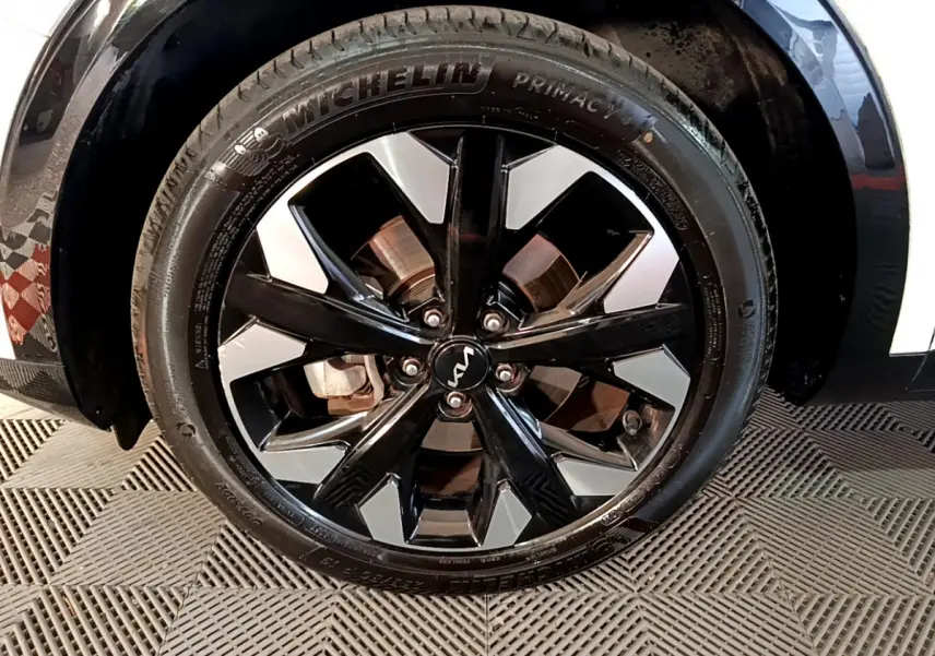 Gros plan sur la roue avant droite du KIA SPORTAGE blanc, jante alliage noir et argent avec logo KIA central.