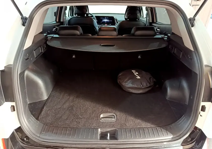 Coffre ouvert d'un KIA SPORTAGE blanc 2022, vue arrière, avec housse ronde noire au sol et banquette arrière visible.