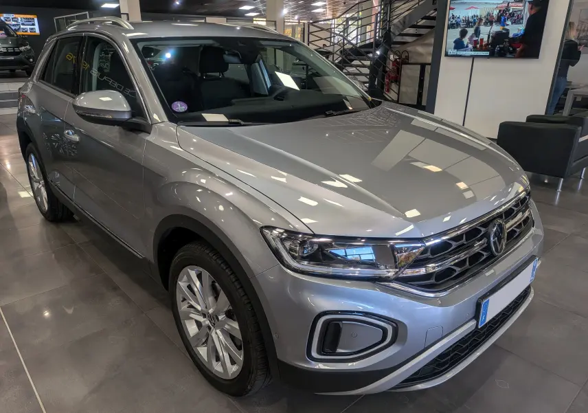 Volkswagen T-Roc gris pyrite en 3/4 avant droit, mettant en valeur ses optiques LED et jantes alliage 18 pouces.