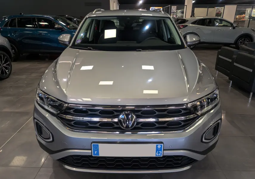 Vue frontale d'un Volkswagen T-Roc 1.5 TSI gris pyrite, mettant en valeur sa calandre chromée et ses phares LED.