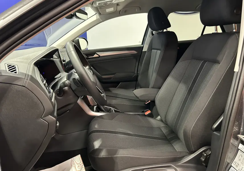 Vue intérieure côté conducteur du Volkswagen T-Roc 2025, sièges tissu noir avec coutures contrastées et tableau de bord moderne.