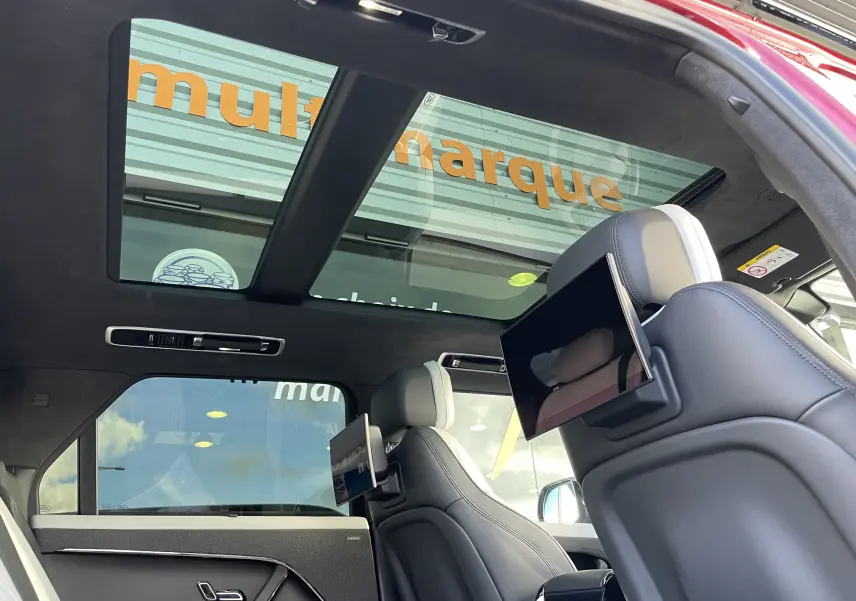 Vue intérieure arrière du Range Rover Sport P440 HSE R-Dynamic rouge, sièges cuir blanc avec écrans TV intégrés et toit panoramique.