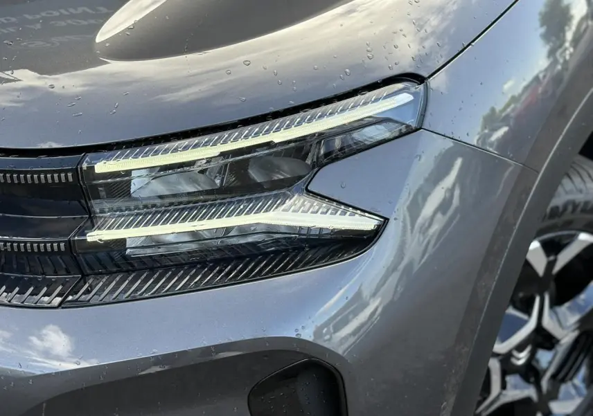 Gros plan sur le phare avant droit allumé du Citroën C5 Aircross 2025 gris Platinium avec jante alliage visible
