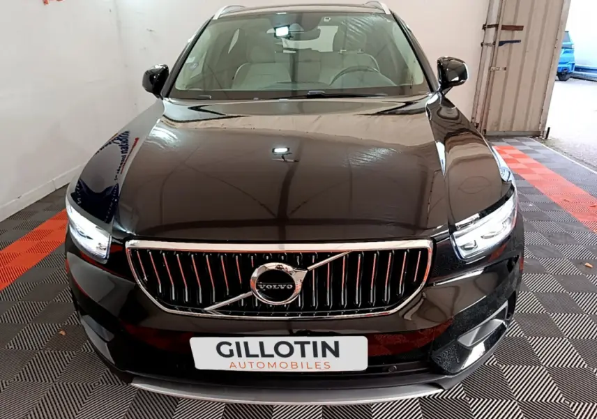 Vue frontale d'un Volvo XC40 noir avec calandre chromée et phares LED allumés dans un showroom.