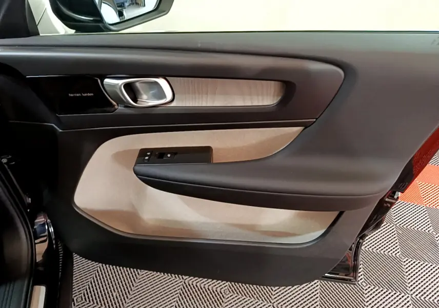 Intérieur côté gauche de la porte d’un Volvo XC40 noir, avec garniture beige et poignée argentée.