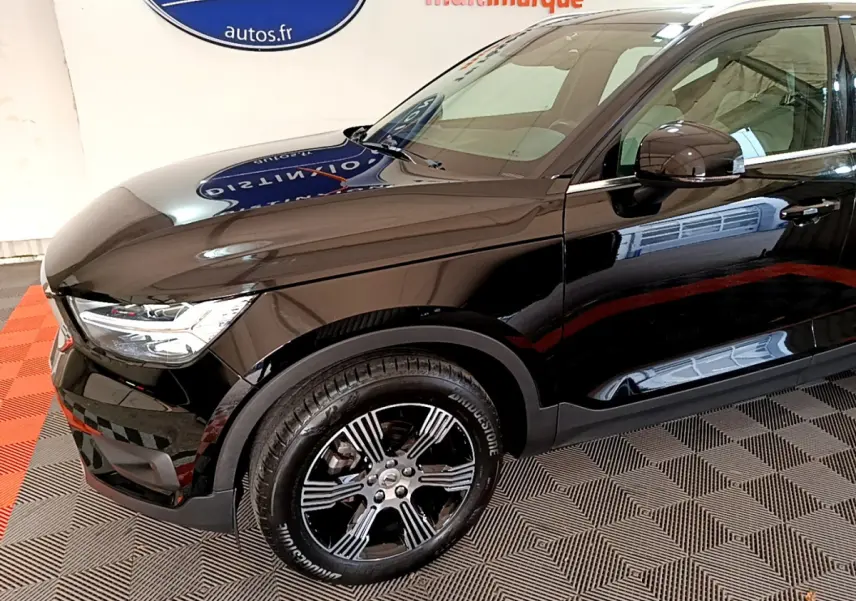 Vue 3/4 avant droit du Volvo XC40 noir brillant, mettant en valeur ses jantes alliage et ses phares LED distinctifs.