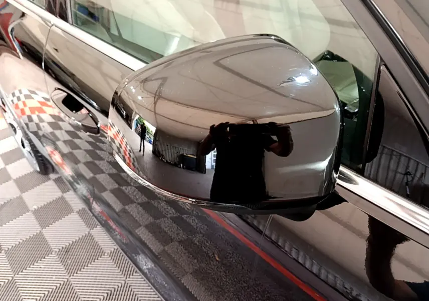 Rétroviseur côté gauche noir brillant d'un Volvo XC40 T3 2020, reflétant l'intérieur d'un garage avec sol damier.