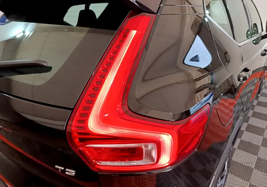 Gros plan sur le feu arrière droit allumé d’un Volvo XC40 T3 noir, reflétant l’éclairage intérieur du garage.