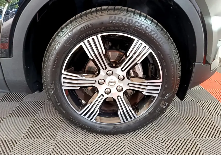 Gros plan sur la roue avant droite du Volvo XC40 noir, mettant en valeur la jante alliage à rayures argentées et pneus Bridgestone.