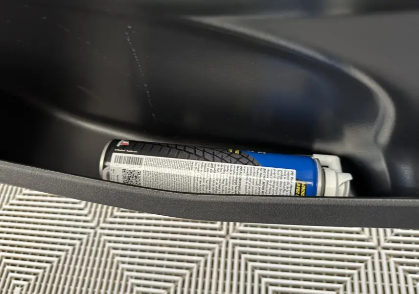 Gros plan sur un produit de réparation de pneus rangé dans le coffre d'une Aixam Ambition 0.5 City Pack gris foncé.