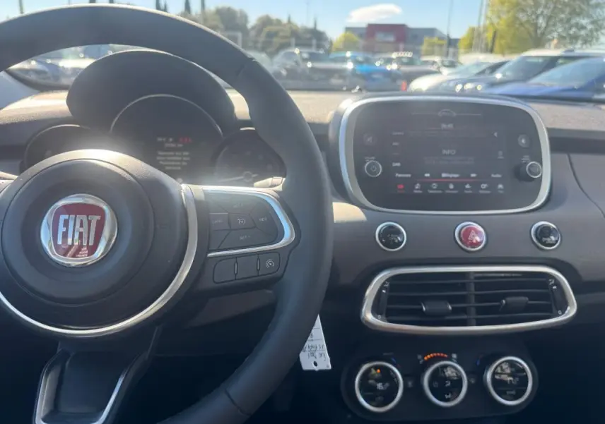 Vue intérieure du tableau de bord et volant FIAT 500X MY23, avec écran tactile et commandes au volant visibles.