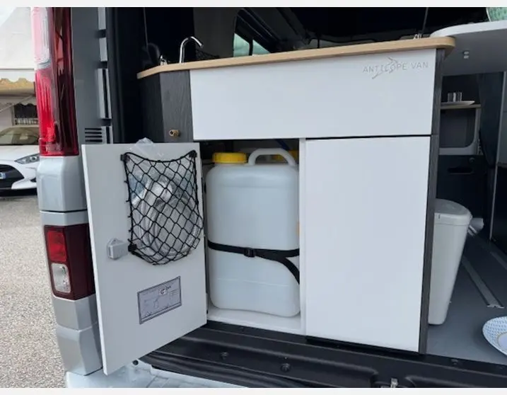 Vue arrière du Renault Trafic Fourgon gris Highland montrant le meuble de cuisine intégré avec porte ouverte et réservoir blanc.