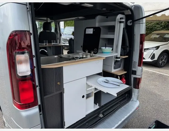 Vue arrière ouverte du Renault Trafic Fourgon gris Highland montrant l'aménagement cuisine intégré avec évier et rangements.