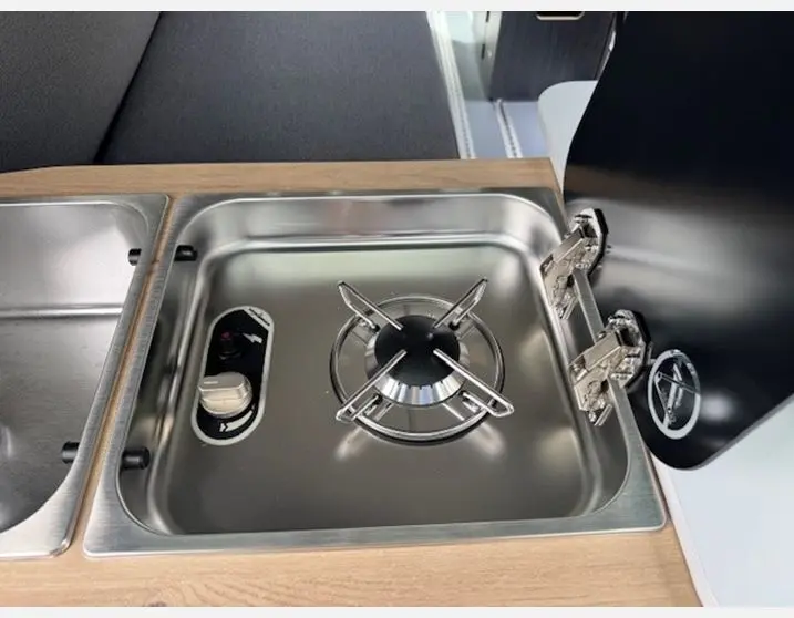 Gros plan sur le réchaud gaz inox intégré au plan de travail bois dans l'aménagement intérieur du Renault Trafic Fourgon gris Highland.