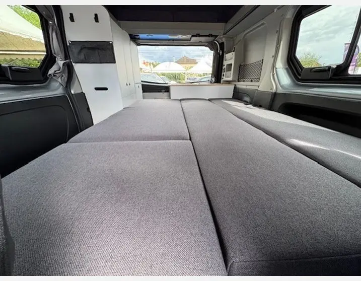Vue intérieure arrière du Renault Trafic Fourgon gris Highland aménagé en couchage avec banquette dépliée et rangements intégrés.