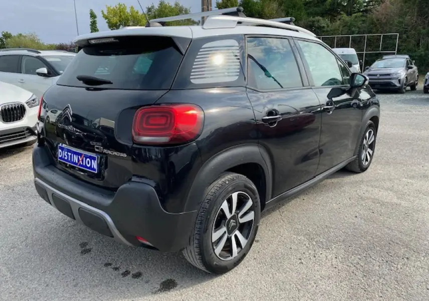 Vue 3/4 arrière droite du Citroën C3 Aircross noir avec toit blanc et jantes bicolores sur parking.