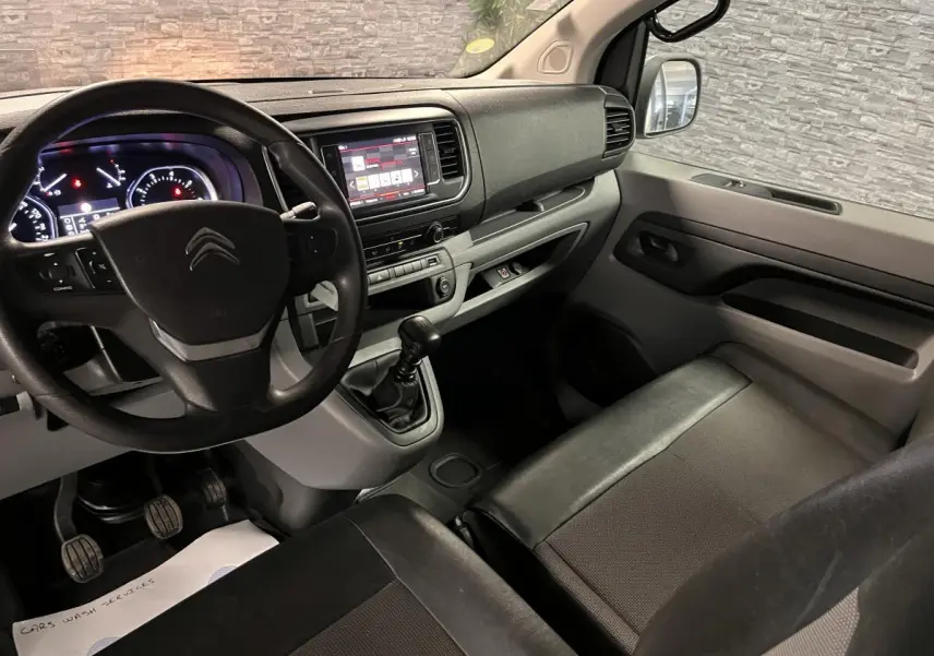 Vue intérieure côté conducteur du Citroën Jumpy blanc, tableau de bord moderne avec volant et boîte manuelle visible.