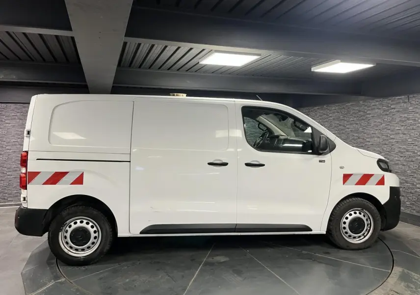 Profil droit d'un utilitaire Citroën Jumpy blanc de 2019 avec bandes réfléchissantes rouges et blanches sur ailes avant et arrière.