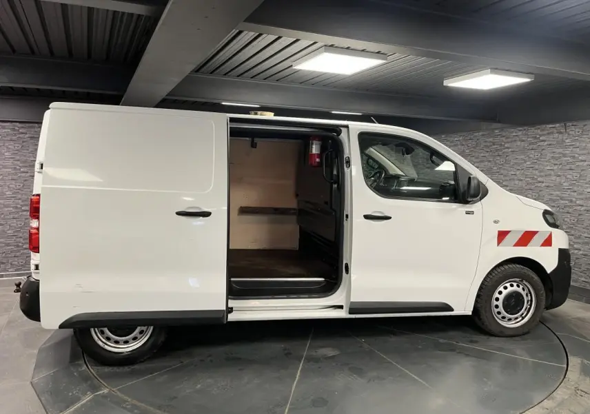 Vue de profil côté droit d'un utilitaire Citroën Jumpy blanc avec porte coulissante ouverte et marquages rouges sur l'aile avant.