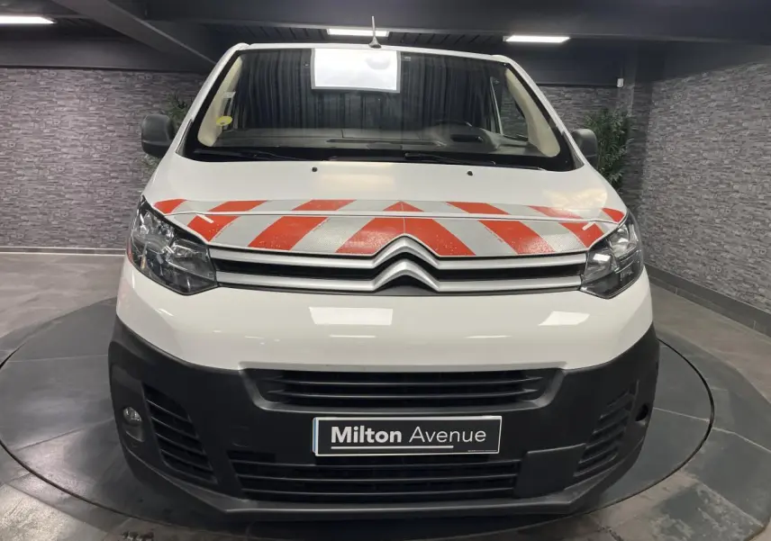 Vue frontale d'un Citroën Jumpy blanc avec bandes rouges réfléchissantes sur le capot et boucliers noirs.