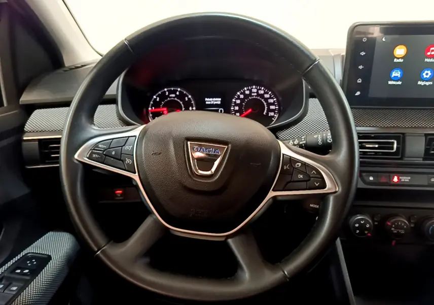 Vue intérieure centrée sur le volant cuir noir avec logo Dacia, tableau de bord et écran tactile du Sandero blanc 2022.