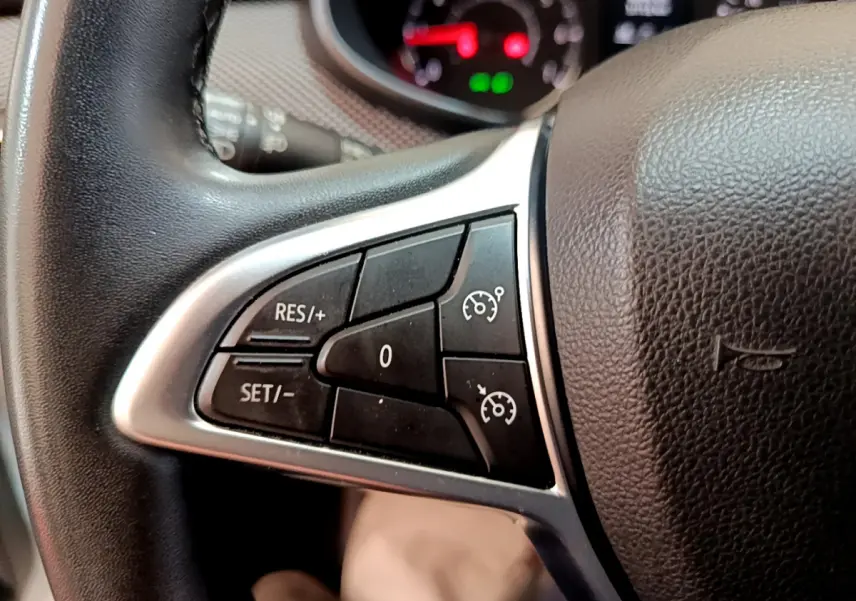 Gros plan sur les commandes du régulateur de vitesse au volant cuir de la Dacia Sandero Confort blanche 2022.