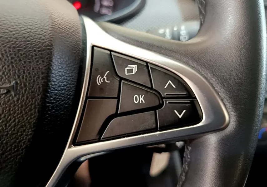 Gros plan sur les commandes multifonctions côté gauche du volant cuir noir de la Dacia Sandero Confort TCe 90 blanche 2022.