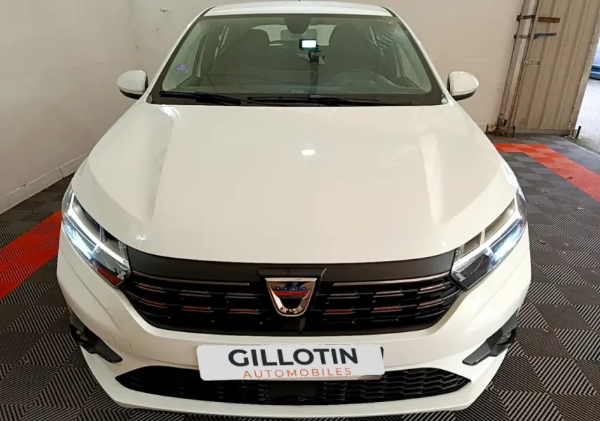 Vue frontale d'une Dacia Sandero Confort TCe 90 blanche avec calandre noire et phares LED allumés.