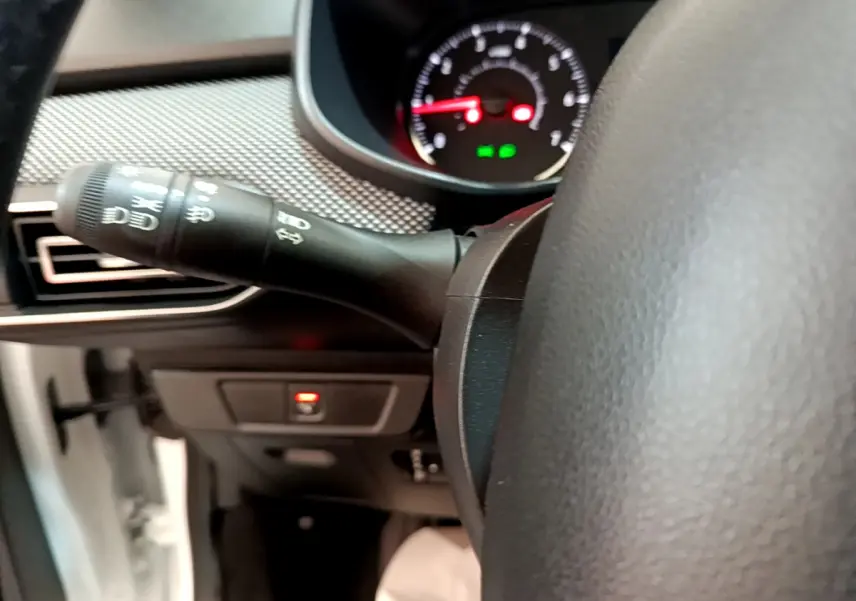 Gros plan sur la manette de clignotant à gauche du volant cuir d'une Dacia Sandero blanche, tableau de bord en arrière-plan.