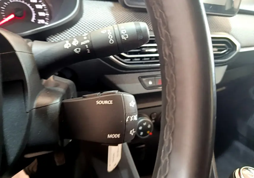 Gros plan sur le volant cuir et commandes multimédia à gauche du tableau de bord d'une Dacia Sandero blanche 2022.