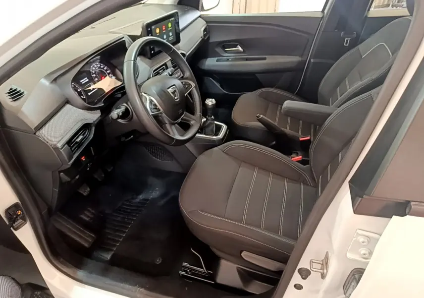 Intérieur de la Dacia Sandero blanc vue côté conducteur, tableau de bord moderne avec écran tactile et volant cuir.