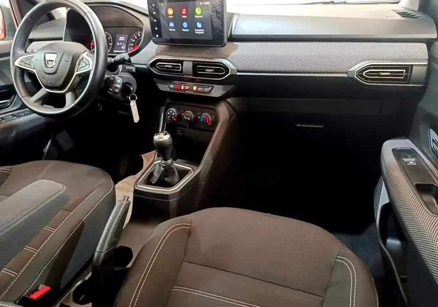 Intérieur noir de la Dacia Sandero 2022 vue côté conducteur, avec tableau de bord central tactile et levier de vitesse manuel.