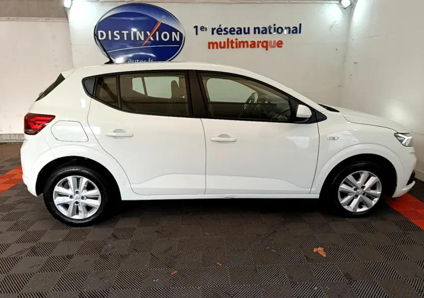 Profil droit d'une Dacia Sandero Confort TCe 90 blanche 2022, stationnée en intérieur sur sol noir et rouge.