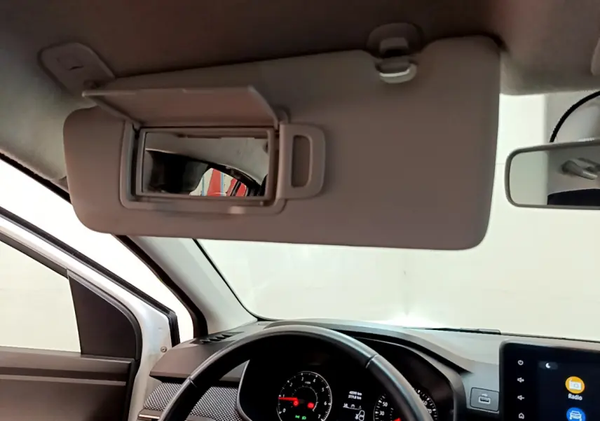 Vue intérieure du tableau de bord et volant cuir noir d'une Dacia Sandero blanche, avec pare-soleil et miroir ouvert.