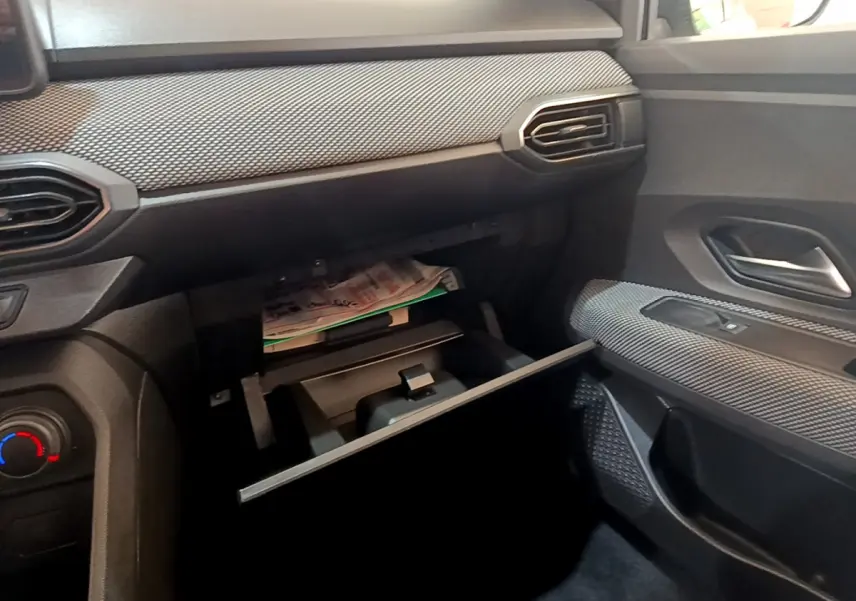 Intérieur côté passager d'une Dacia Sandero blanc 2022, boîte à gants ouverte avec documents visibles.