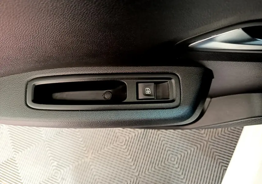 Gros plan sur la poignée intérieure noire et l'interrupteur de lève-vitre côté conducteur d'une Dacia Sandero blanche.