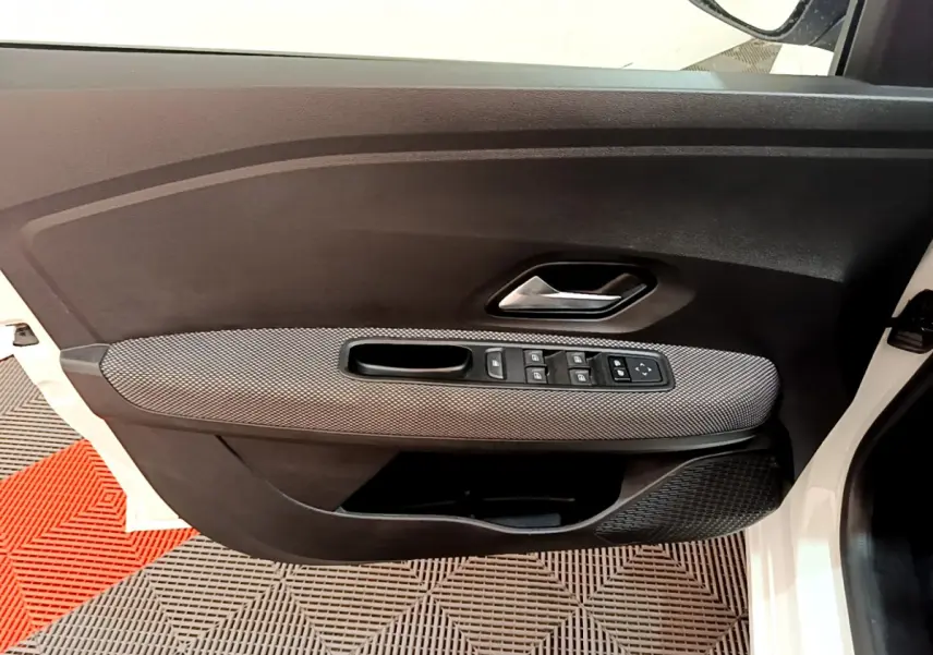 Vue intérieure côté gauche de la porte avant blanche de la Dacia Sandero Confort TCe 90 avec commandes de vitres et poignée chrome.