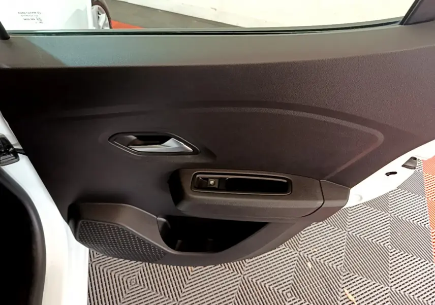 Détail de la porte intérieure côté gauche d'une Dacia Sandero blanche, avec poignée et commande de vitre électrique.