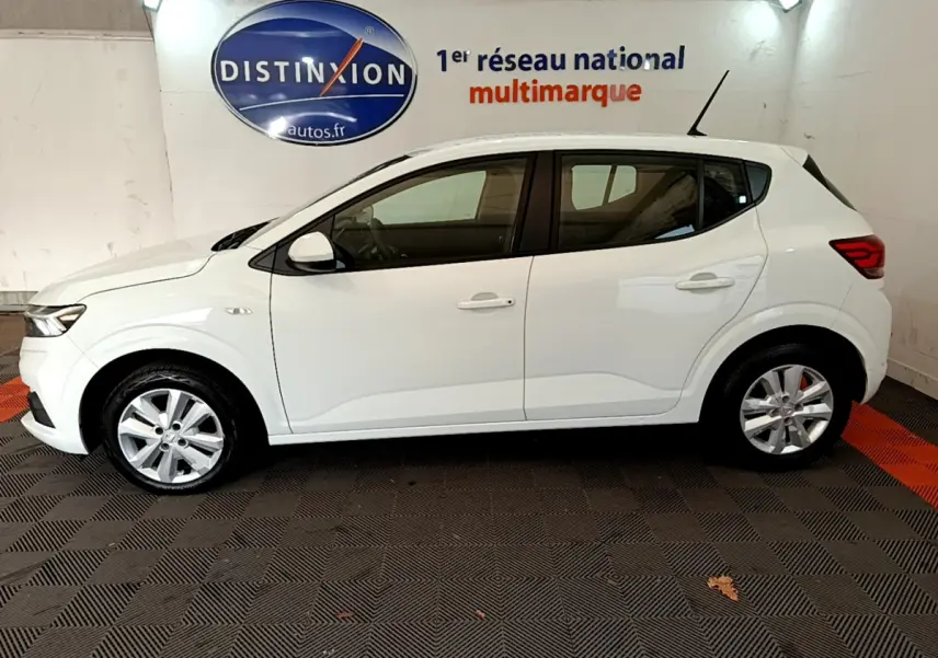 Profil côté gauche d'une Dacia Sandero Confort TCe 90 blanche de 2022, stationnée en intérieur sur sol à damiers.