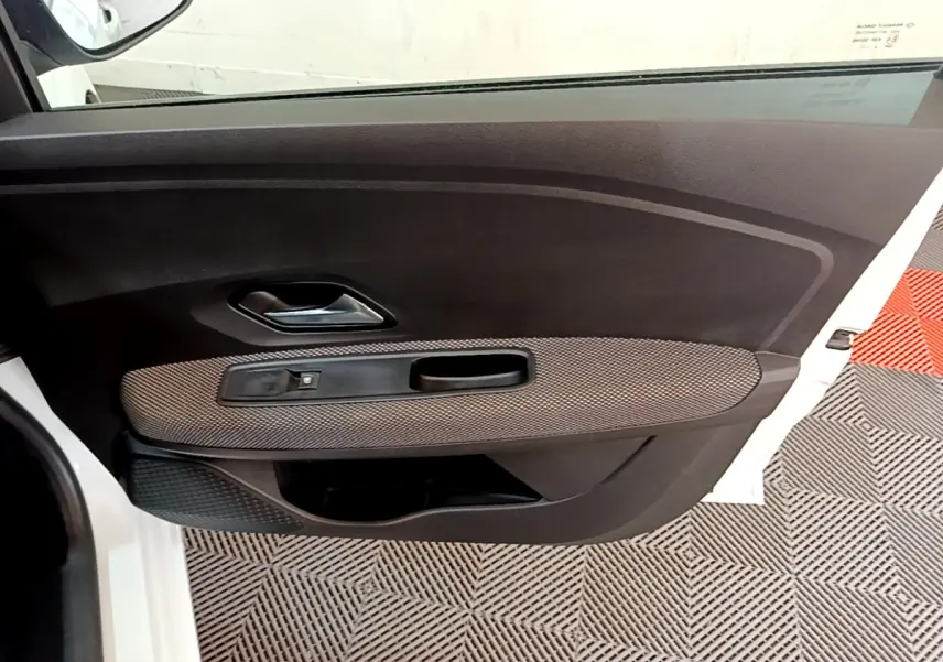 Vue intérieure de la porte avant gauche blanche d'une Dacia Sandero Confort TCe 90 avec poignée et commande de vitre.