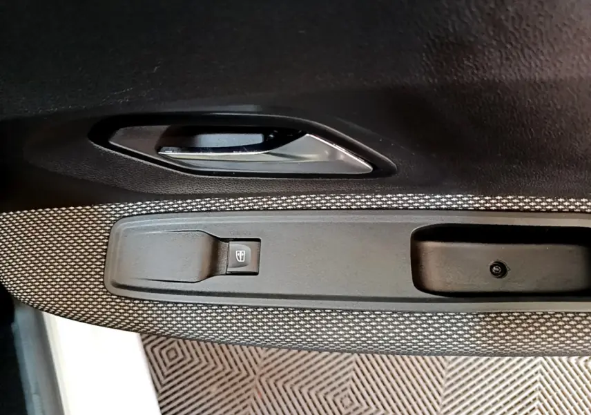 Gros plan sur la poignée intérieure et le bouton de lève-vitre côté gauche de la porte d'une Dacia Sandero blanche.