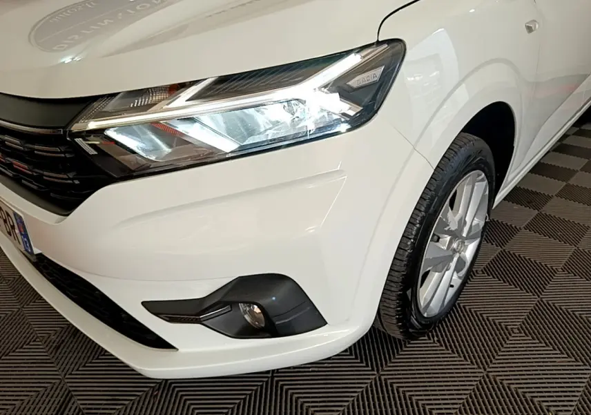 Vue 3/4 avant droit d'une Dacia Sandero Confort TCe 90 blanche, mettant en valeur le phare LED et la calandre noire.