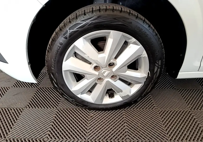 Gros plan sur la roue avant gauche d'une Dacia Sandero blanche, jante alliage avec logo central visible.