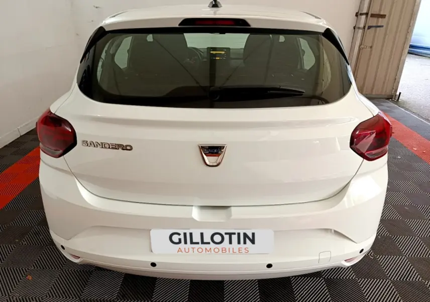 Vue arrière d'une Dacia Sandero blanche 2022 avec feux rouges et logo centré sur un sol à damiers noir et rouge.