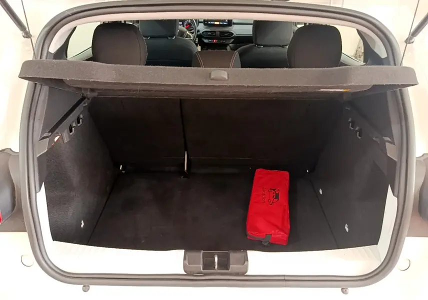 Coffre ouvert d'une Dacia Sandero blanche 2022, montrant l'intérieur noir avec une trousse de secours rouge.