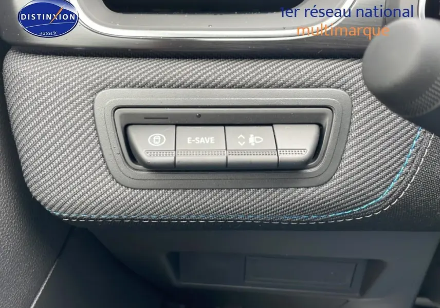 Gros plan sur les commandes E-Save et réglage des phares sur tableau de bord en tissu gris avec surpiqûres bleues.