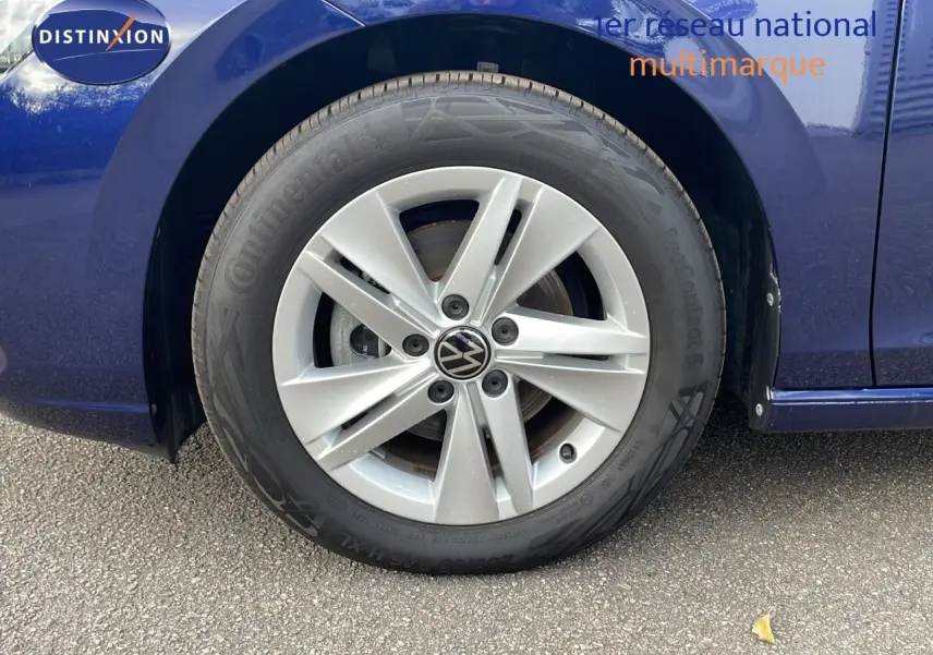 Gros plan sur la roue avant gauche d'une Volkswagen Golf VIII bleu lapiz metal avec jante alliage cinq branches.