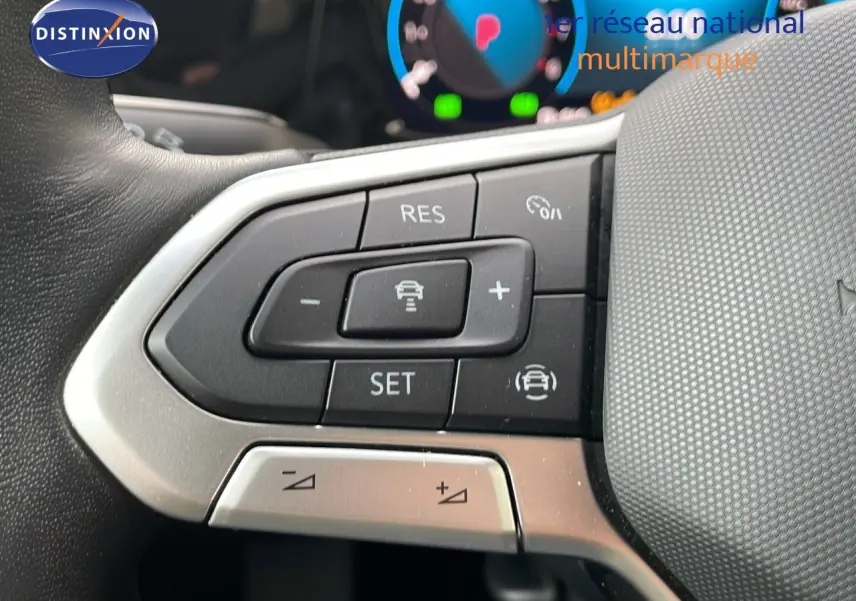 Gros plan sur les commandes au volant côté gauche d'une Volkswagen Golf VIII bleu lapiz metal, avec tableau de bord numérique flou.