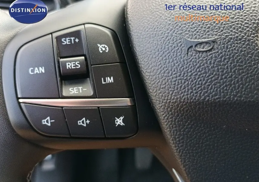 Gros plan sur les commandes de régulateur de vitesse et volume audio au volant noir du Ford Puma gris foncé 2023.